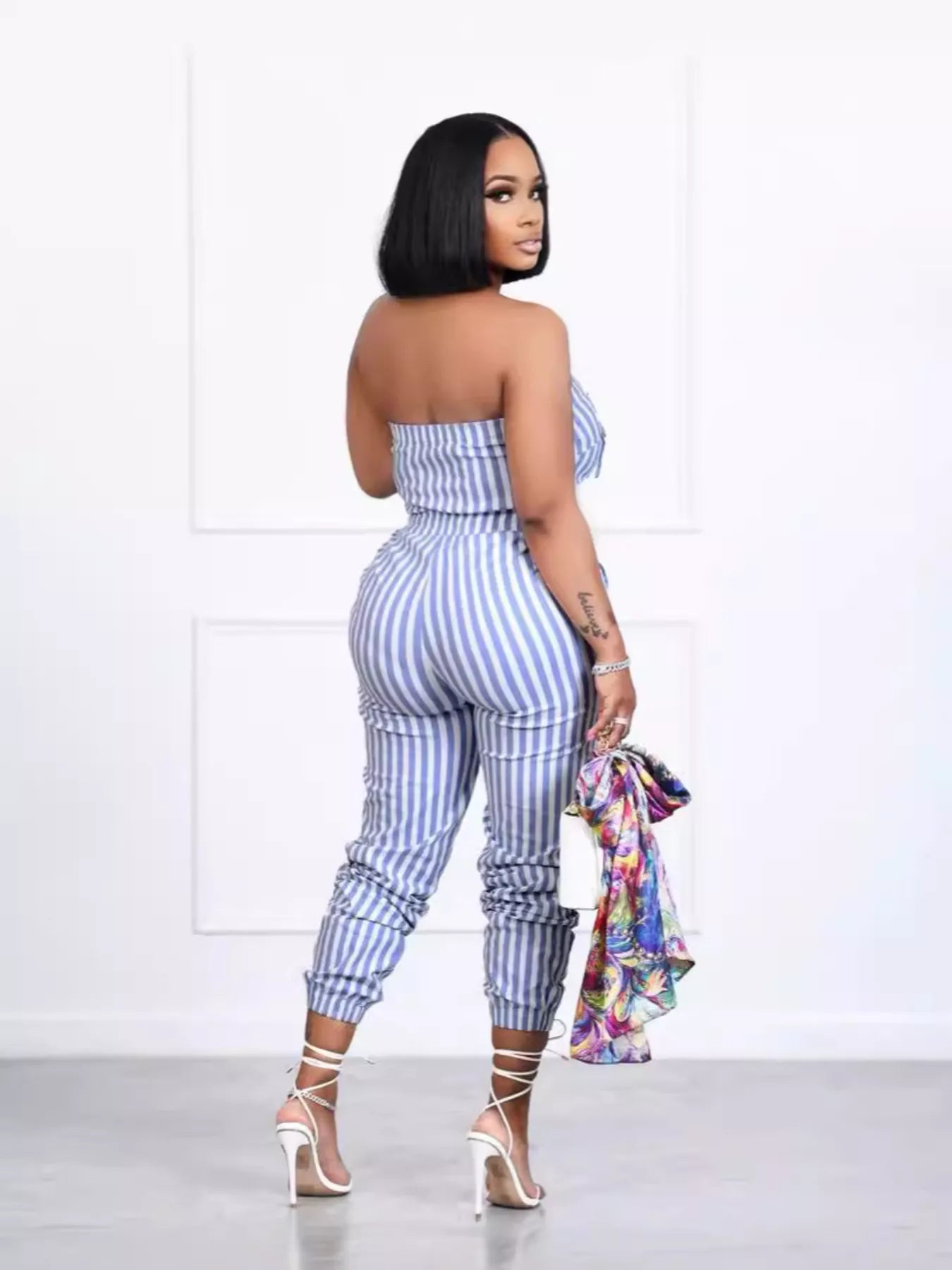 Striped blue-and-white tube jumpsuit with pockets, fitted waist, back view, white strappy heels.